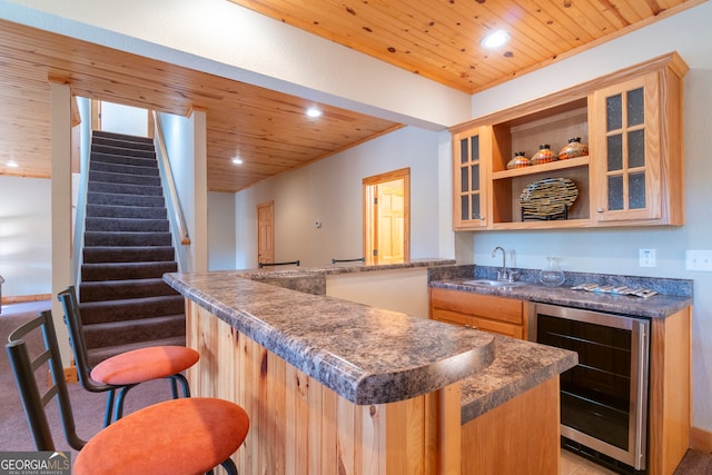 bar with light brown cabinetry, sink, beverage cooler, and wood ceiling