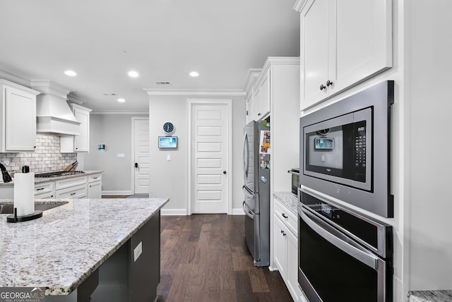 kitchen with white cabinets, dark hardwood / wood-style floors, crown molding, light stone countertops, and appliances with stainless steel finishes