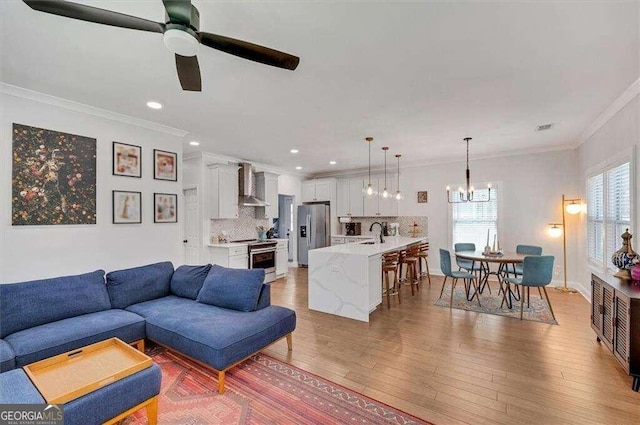 living room featuring a wealth of natural light, ceiling fan with notable chandelier, light wood-type flooring, and crown molding