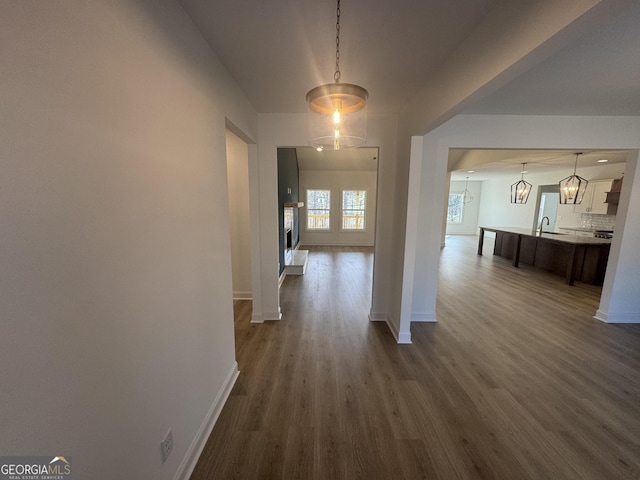 hallway with dark wood-type flooring, a chandelier, and sink