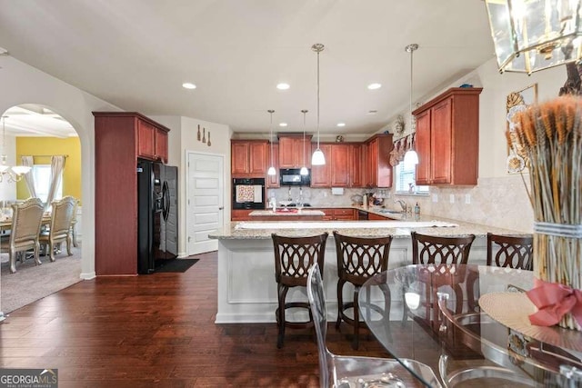 kitchen featuring arched walkways, decorative backsplash, decorative light fixtures, a peninsula, and black appliances