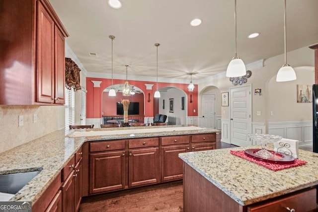 kitchen featuring a wainscoted wall, a kitchen island, arched walkways, and decorative light fixtures