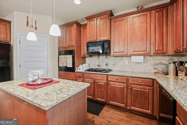 kitchen with black appliances, light stone countertops, decorative light fixtures, light hardwood / wood-style flooring, and a kitchen island