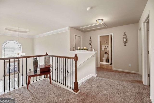 corridor featuring attic access, baseboards, ornamental molding, an upstairs landing, and carpet floors