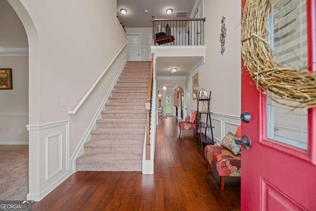 entrance foyer featuring arched walkways, a decorative wall, dark wood-style flooring, and crown molding