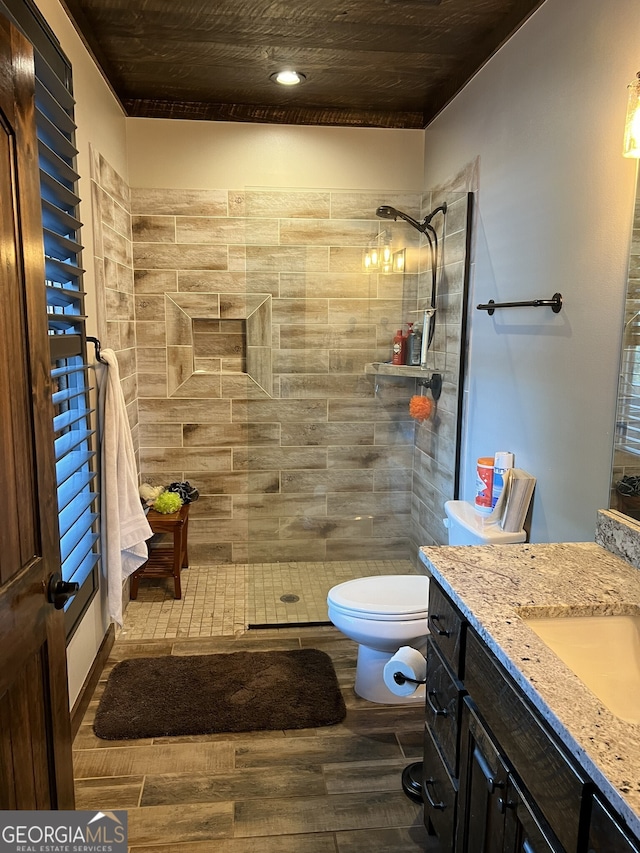 bathroom featuring toilet, vanity, hardwood / wood-style flooring, and a tile shower