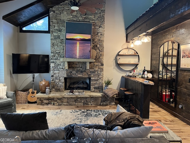 living room with ceiling fan, high vaulted ceiling, hardwood / wood-style floors, a fireplace, and indoor bar