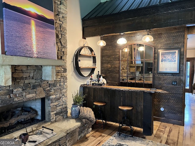 bar with a stone fireplace, hanging light fixtures, and hardwood / wood-style floors