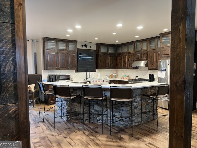 kitchen with dark brown cabinetry, light hardwood / wood-style floors, a breakfast bar area, and appliances with stainless steel finishes