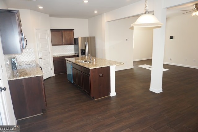 kitchen featuring dark wood-type flooring, appliances with stainless steel finishes, decorative light fixtures, and an island with sink