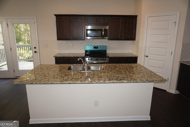 kitchen featuring sink, appliances with stainless steel finishes, light stone countertops, dark hardwood / wood-style floors, and a kitchen island with sink