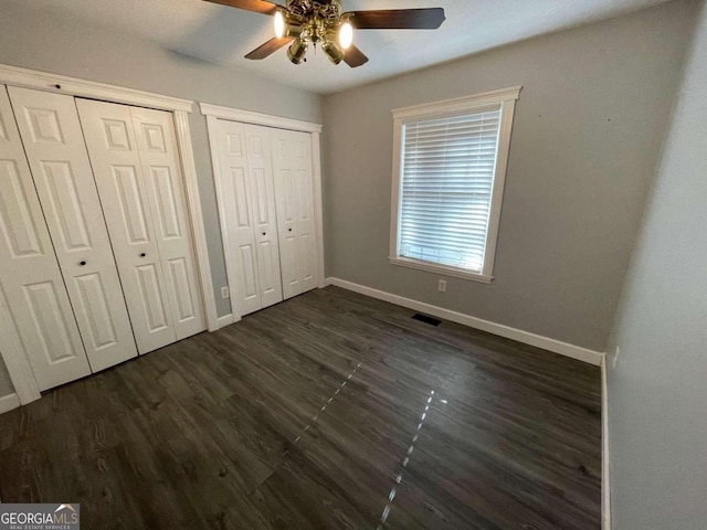 unfurnished bedroom featuring multiple closets, dark hardwood / wood-style flooring, and ceiling fan