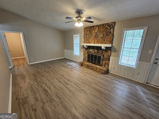 unfurnished living room featuring a stone fireplace, wood-type flooring, ceiling fan, and a textured ceiling