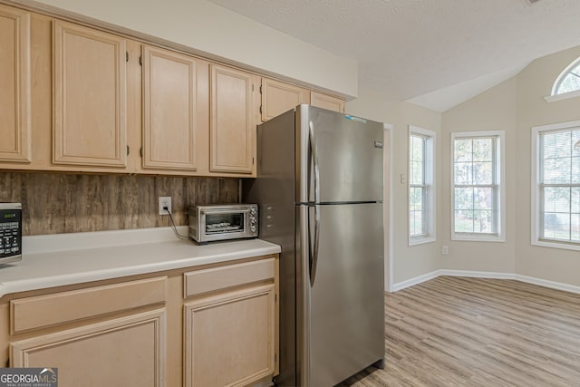 kitchen featuring stainless steel appliances, vaulted ceiling, a textured ceiling, light wood-type flooring, and light brown cabinetry