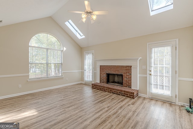 unfurnished living room with ceiling fan, a wealth of natural light, a brick fireplace, and light hardwood / wood-style flooring