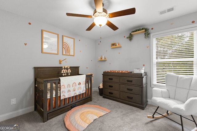 carpeted bedroom featuring a crib and ceiling fan