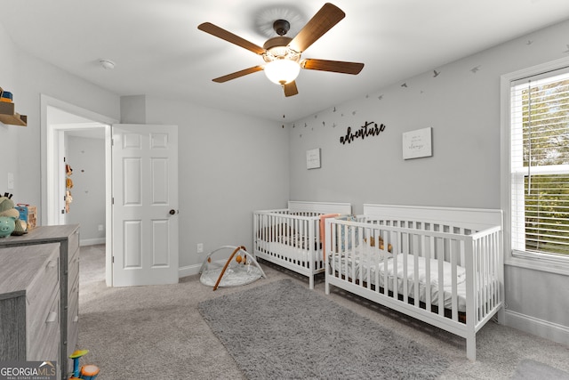 carpeted bedroom featuring ceiling fan and a crib