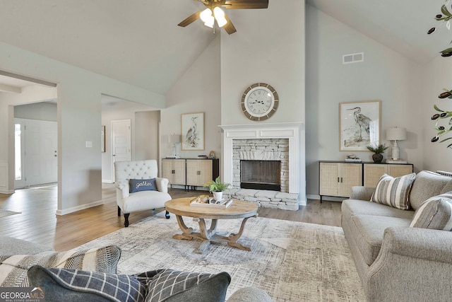 living room with ceiling fan, light hardwood / wood-style floors, a stone fireplace, and high vaulted ceiling