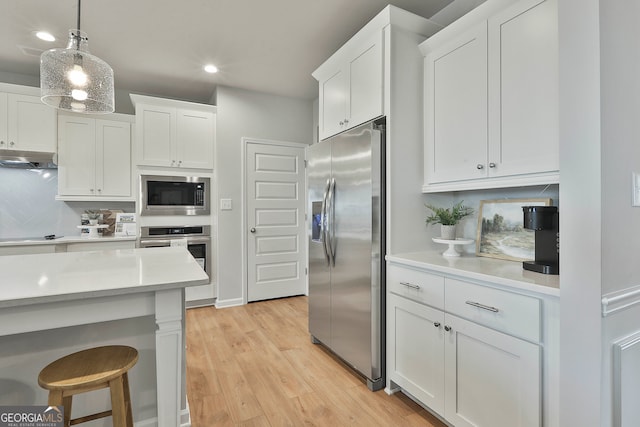 kitchen with white cabinetry, decorative light fixtures, appliances with stainless steel finishes, and light hardwood / wood-style flooring