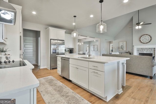 kitchen featuring stainless steel appliances, white cabinetry, sink, an island with sink, and a fireplace