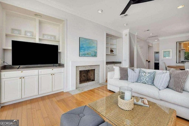 living room with light hardwood / wood-style floors, built in features, ceiling fan, and crown molding