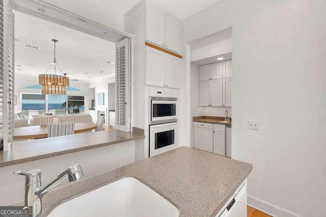 kitchen with sink, white cabinetry, hanging light fixtures, and stainless steel appliances