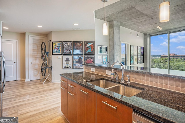 kitchen with pendant lighting, light wood-type flooring, dark stone counters, and sink