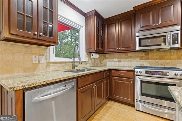 kitchen with backsplash, sink, light stone countertops, light wood-type flooring, and stainless steel appliances