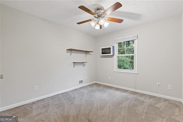 unfurnished room with a textured ceiling, ceiling fan, and light carpet