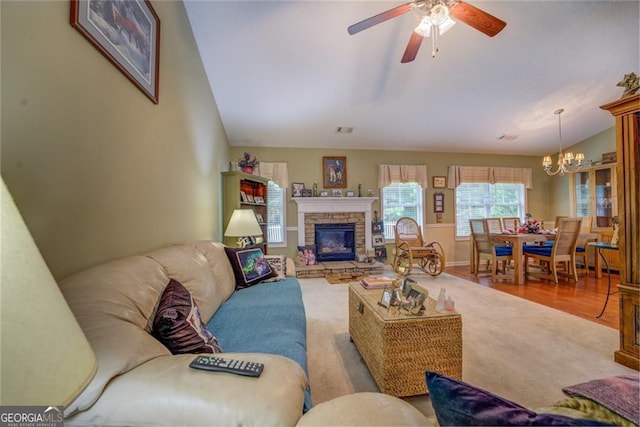 living room with a stone fireplace, ceiling fan with notable chandelier, wood-type flooring, and vaulted ceiling