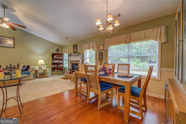 dining space with wood-type flooring, ceiling fan with notable chandelier, and lofted ceiling