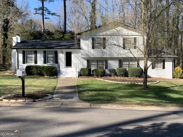 split level home with a front yard, a chimney, and brick siding