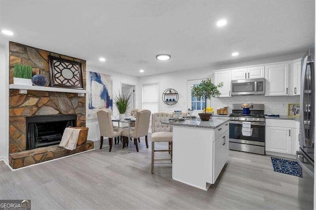 kitchen featuring stainless steel appliances, a stone fireplace, a kitchen island, white cabinetry, and light hardwood / wood-style flooring