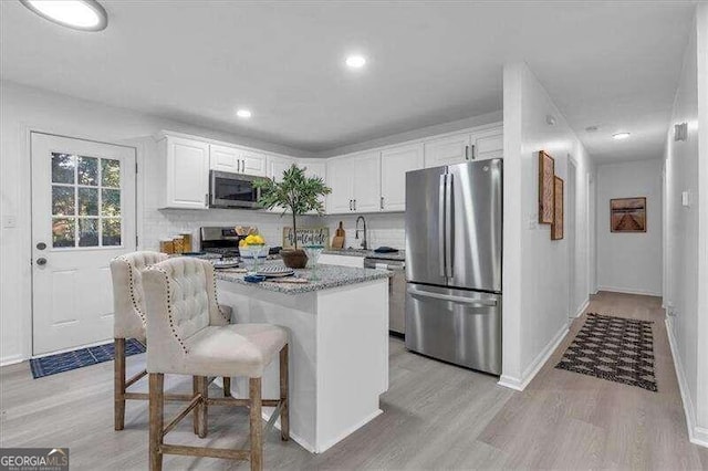 kitchen with stainless steel appliances, light hardwood / wood-style floors, stone countertops, white cabinetry, and a kitchen bar