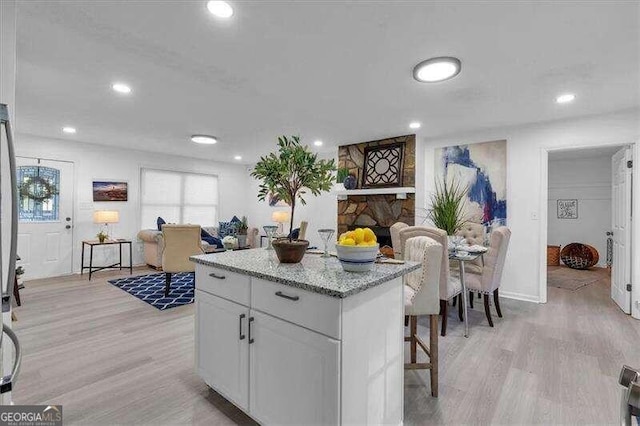 kitchen with white cabinets, light stone countertops, a kitchen breakfast bar, light hardwood / wood-style floors, and a center island