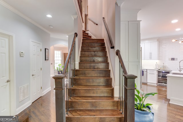 stairway featuring beverage cooler, sink, hardwood / wood-style flooring, and crown molding