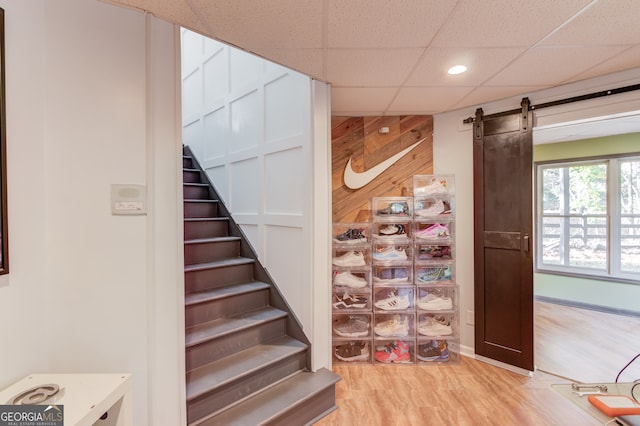 stairway with wood walls, a paneled ceiling, a barn door, and hardwood / wood-style flooring