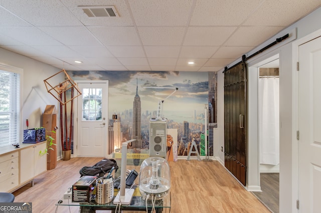 dining space featuring a barn door, plenty of natural light, light wood-type flooring, and a drop ceiling