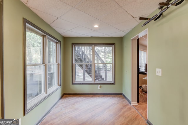 empty room with light hardwood / wood-style floors, plenty of natural light, and a drop ceiling