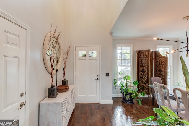 entryway featuring dark wood-type flooring, crown molding, and a notable chandelier