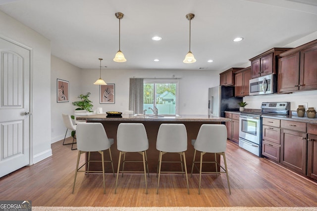 kitchen with pendant lighting, a kitchen island, appliances with stainless steel finishes, and hardwood / wood-style flooring