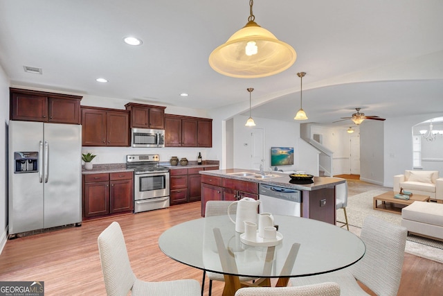 kitchen featuring pendant lighting, appliances with stainless steel finishes, sink, light wood-type flooring, and a center island with sink