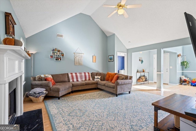 living room featuring a textured ceiling, light hardwood / wood-style floors, high vaulted ceiling, and ceiling fan