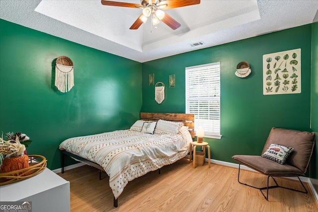 bedroom with wood-type flooring, a textured ceiling, a tray ceiling, and ceiling fan