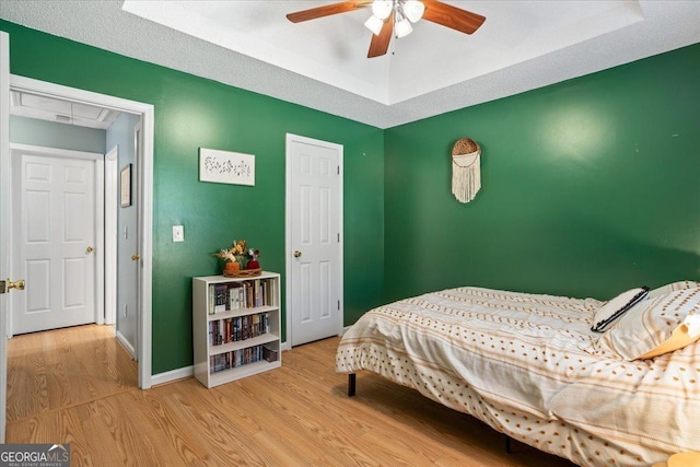 bedroom featuring ceiling fan, light wood-type flooring, and a tray ceiling