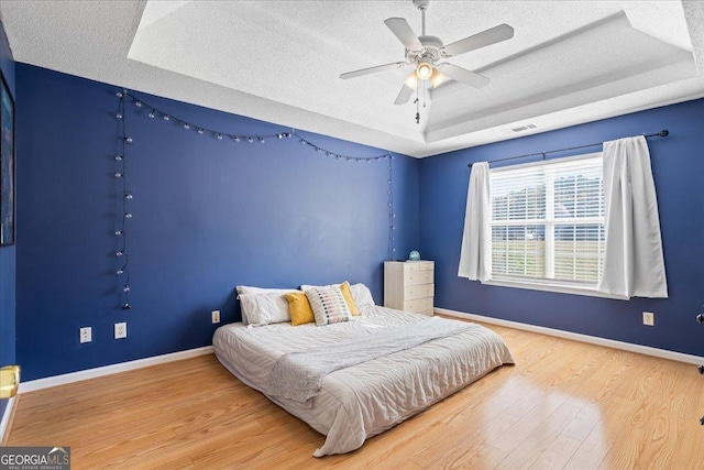 bedroom with ceiling fan, wood-type flooring, a textured ceiling, and a tray ceiling