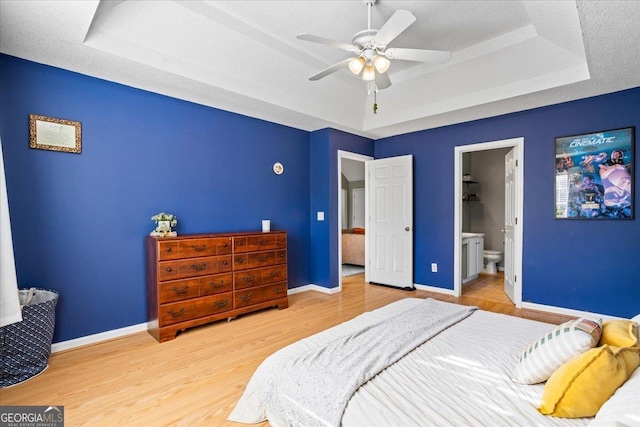 bedroom with connected bathroom, ceiling fan, a raised ceiling, a textured ceiling, and hardwood / wood-style flooring