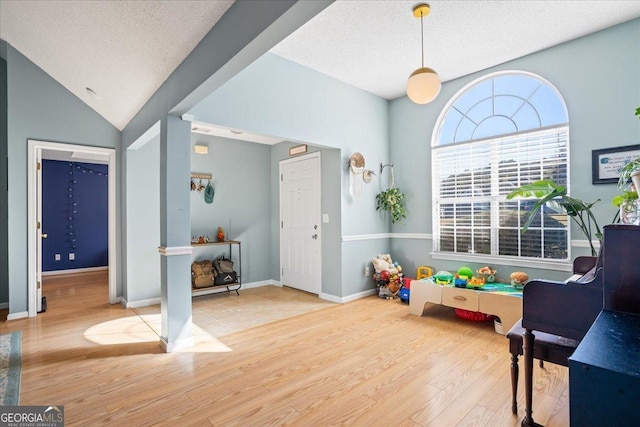 recreation room featuring hardwood / wood-style flooring, lofted ceiling, and a textured ceiling