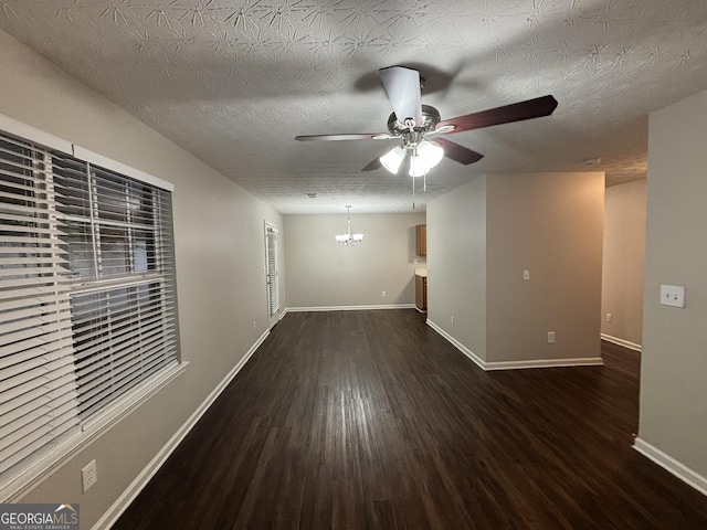 spare room with ceiling fan with notable chandelier, dark wood-type flooring, and a textured ceiling