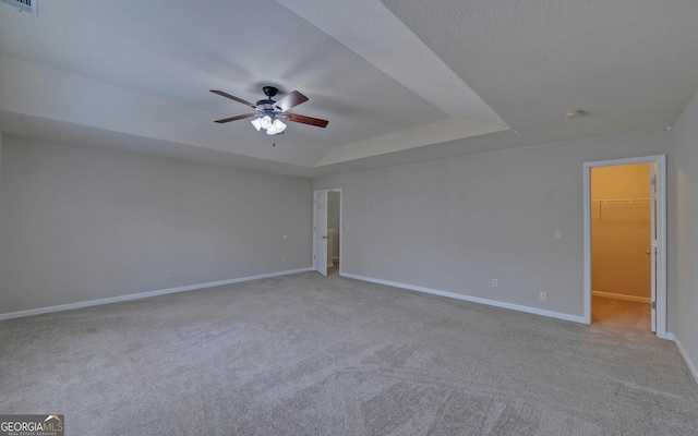 empty room featuring a tray ceiling, a textured ceiling, light colored carpet, and ceiling fan